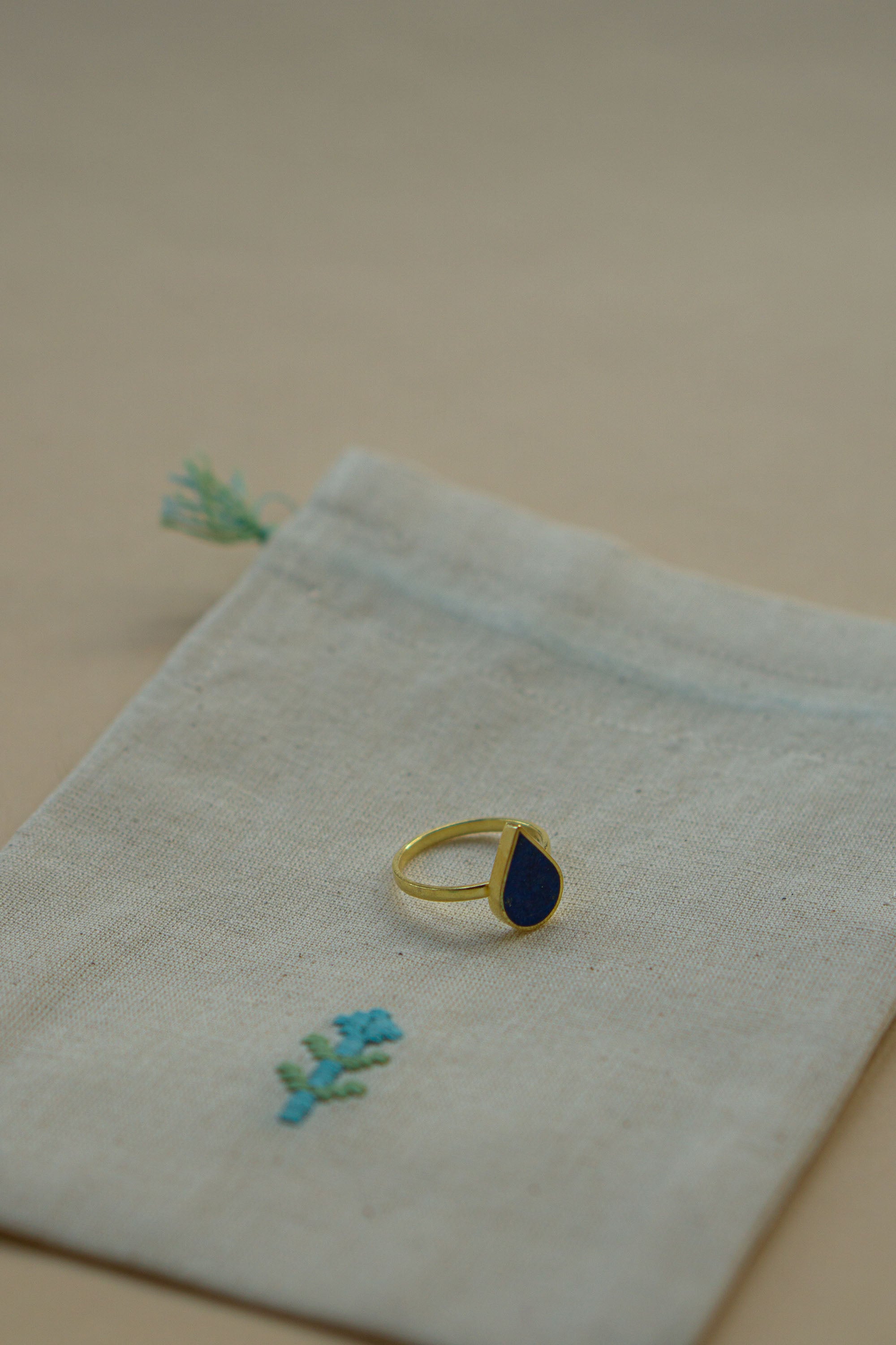 Dråbeformet ring i 24 karat forgyldt sølv med en smuk lapis lazuli sten, håndlavet i Afghanistan. Ringen ligger på en broderet stofpose skabt af afghanske kvinder.