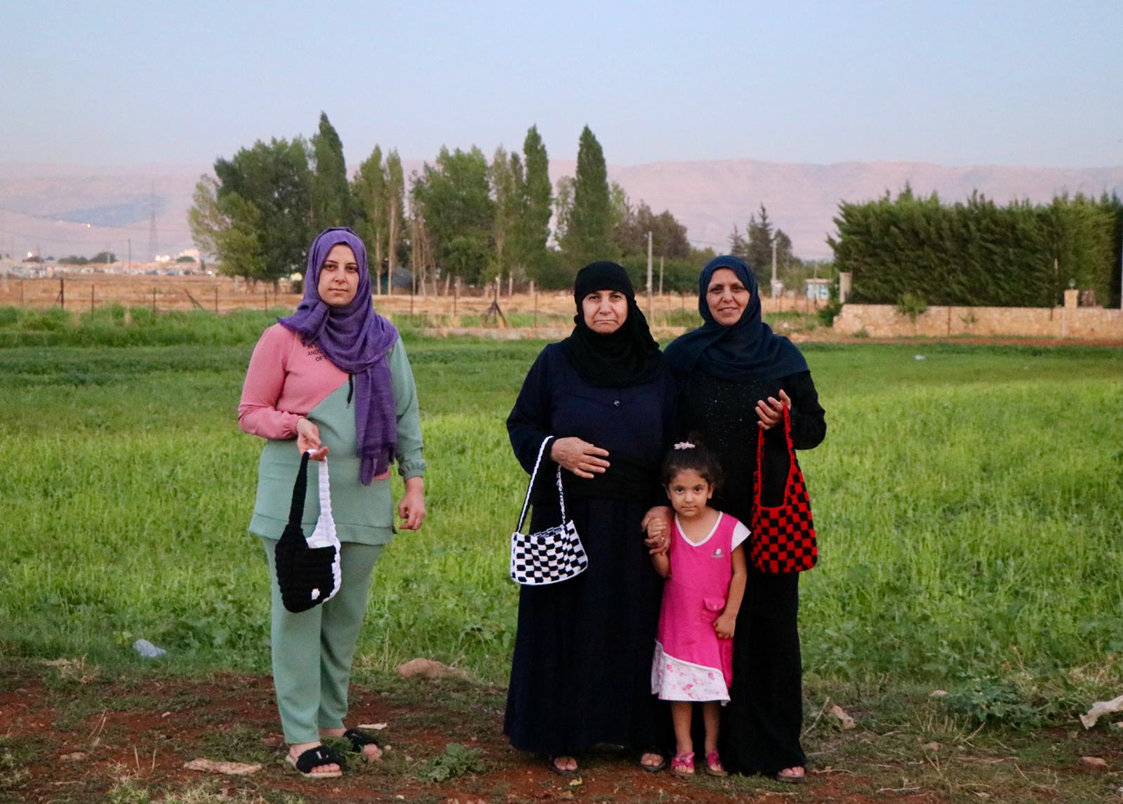 Kvinder fra kvinde-kollektivet Lamsa i Bekaa dalen med hæklede tasker. Billedet viser tre kvinder og et barn stående på en mark, hvor kvinderne holder deres håndlavede tasker.