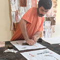 Shadi håndtrykker en dækkeserviet i 100% rest-hør med traditionelle syriske blokprint i sit designstudie i Beirut. De detaljerede mønstre trykkes med hundredårige træstempler fra Damascus, som han og hans bror har hentet. Bag ham hænger tidligere designs og eksperimenter med blokprint.